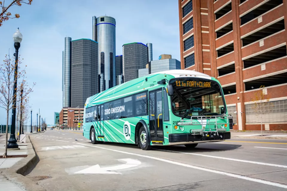 Green Detroit public transit electric bus with high-rise modenr building in background.